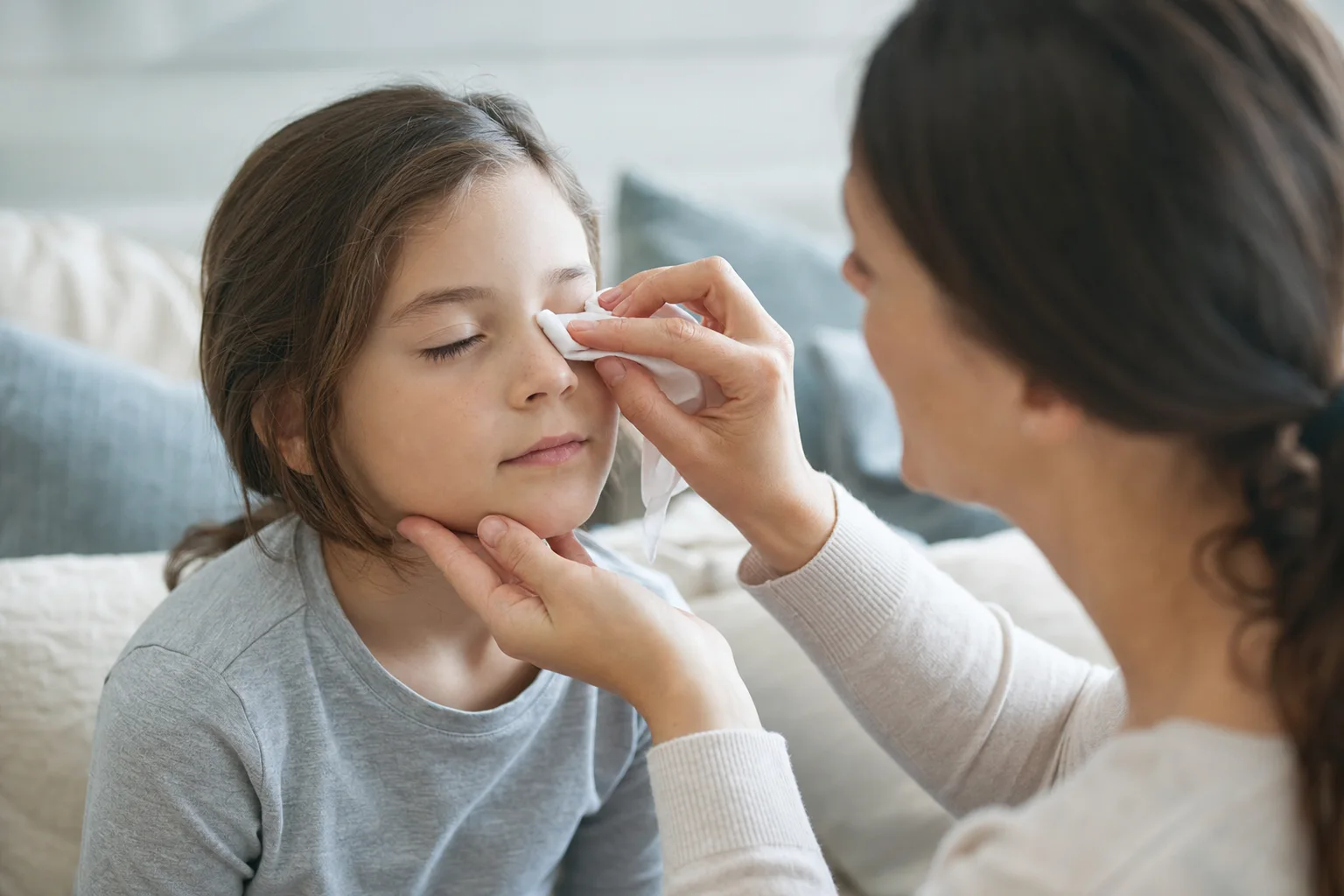 Eltern reinigen das verklebte Auge mit einem frischen Tuch