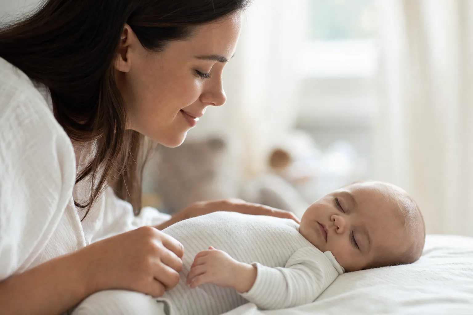 Elternteil schaut ein schlafendes Baby liebevoll an