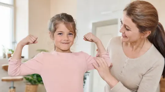 Zuversichtliches Kind, Elternteil steht ermutigend daneben