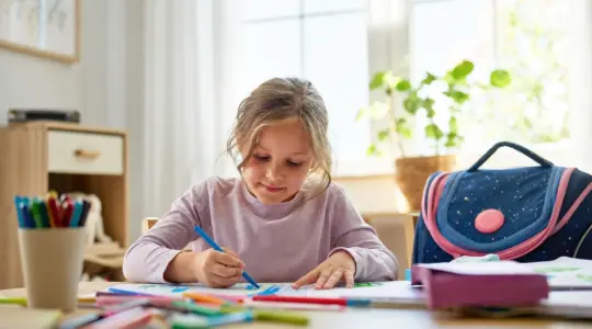 Vorschulkind bastelt konzentriert, ein Schulranzen steht bereit
