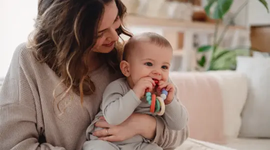 Mutter hält ihr Baby, das auf einem Beißring kaut
