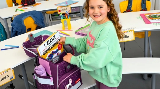 Lachendes Schulkind im Klassenzimmer packt seinen Step by Step SPACE Schulranzen - Schulstart-Gewinnspiel